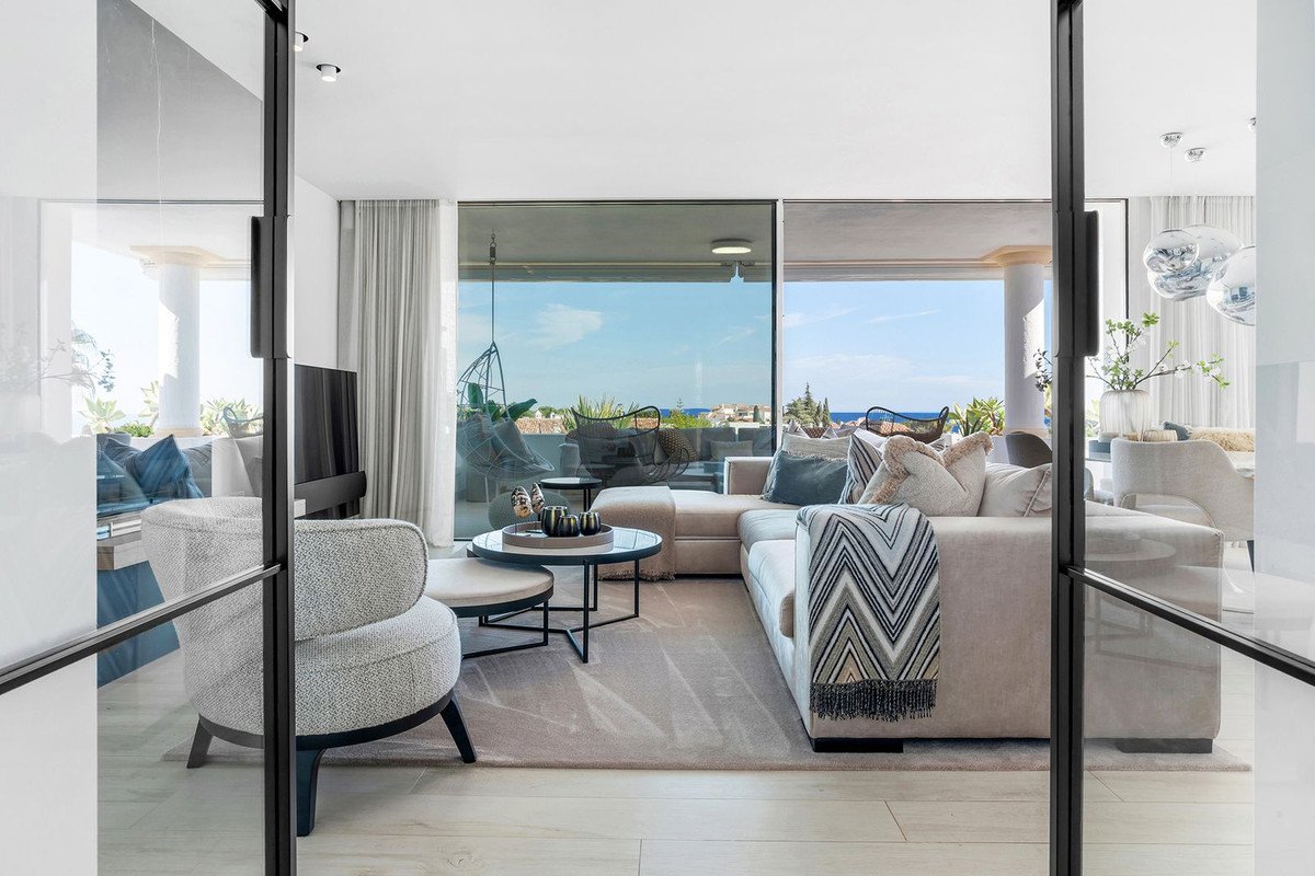 Modern living room with sectional sofa, hanging chair on balcony, and panoramic sea view through large glass windows.