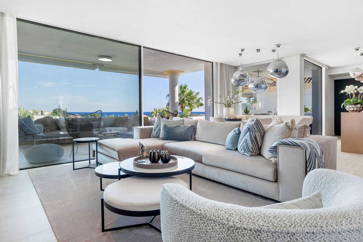 Spacious living room with a large sectional sofa, coffee tables, and panoramic windows offering a sea view and terrace access.