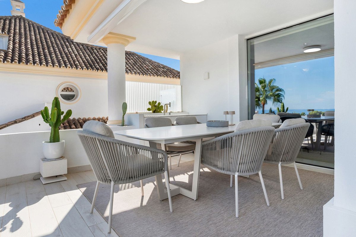 Modern terrace dining set with chairs and table, featuring a view of the sea and palm trees through a large window.