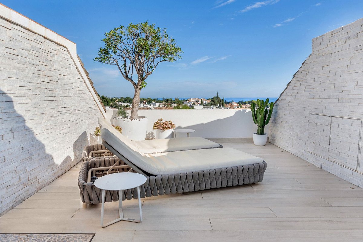 Modern terrace with lounge chairs, a tree, a cactus, and distant sea views under a clear blue sky.