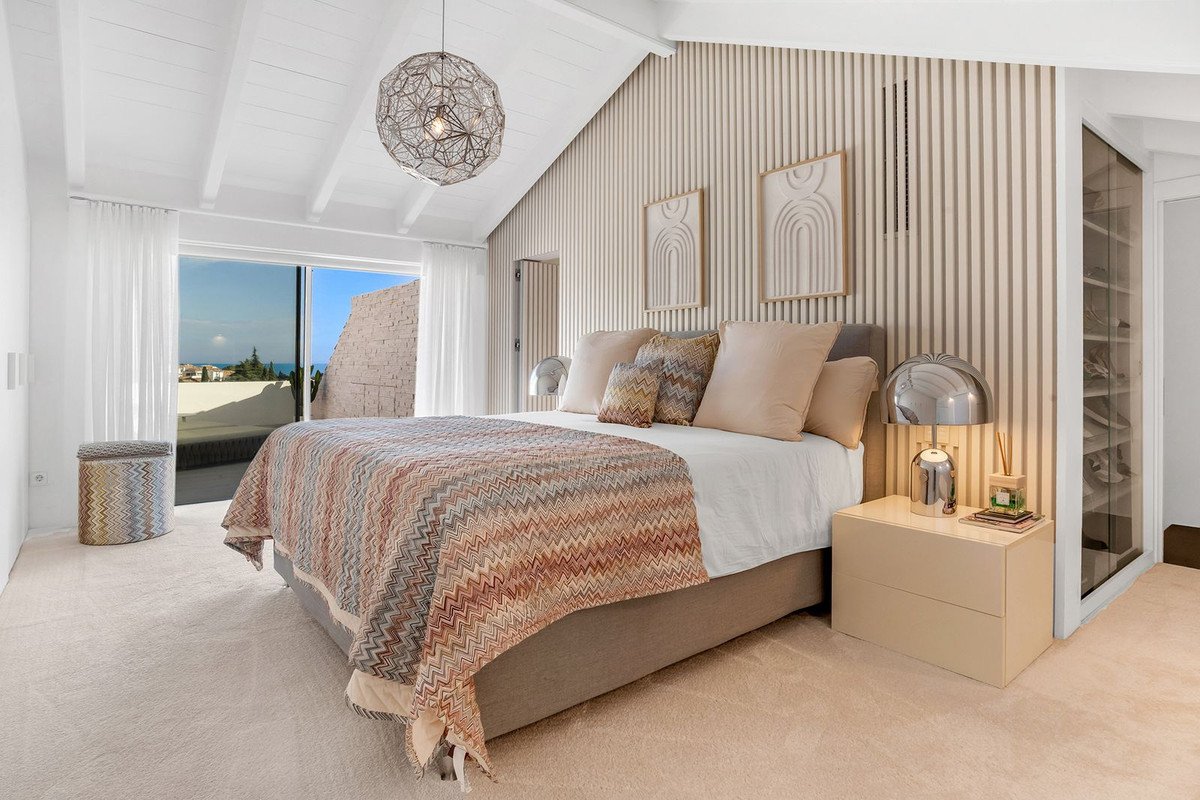 Bedroom with a king-size bed, patterned throw, large windows with sea view, and a walk-in closet.