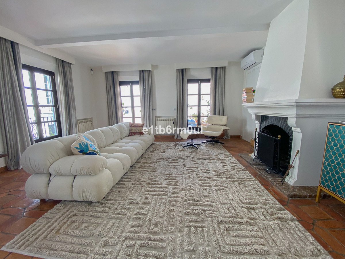 Spacious living room with a long sectional sofa, a fireplace, large windows, and a patterned rug.