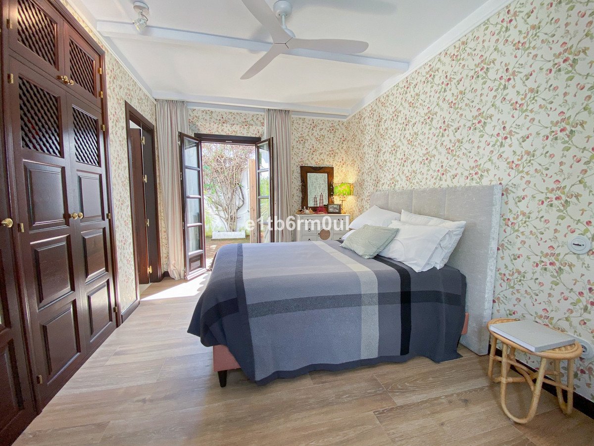 Cozy bedroom with floral wallpaper, large wardrobe, and double doors opening to a garden patio.