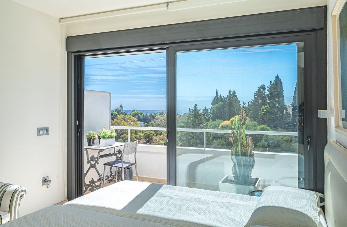 Bedroom with balcony overlooking sea and trees, featuring a bed and outdoor seating