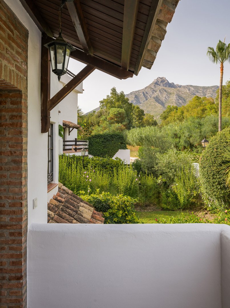 Balcony view of a villa with lush garden and mountain backdrop