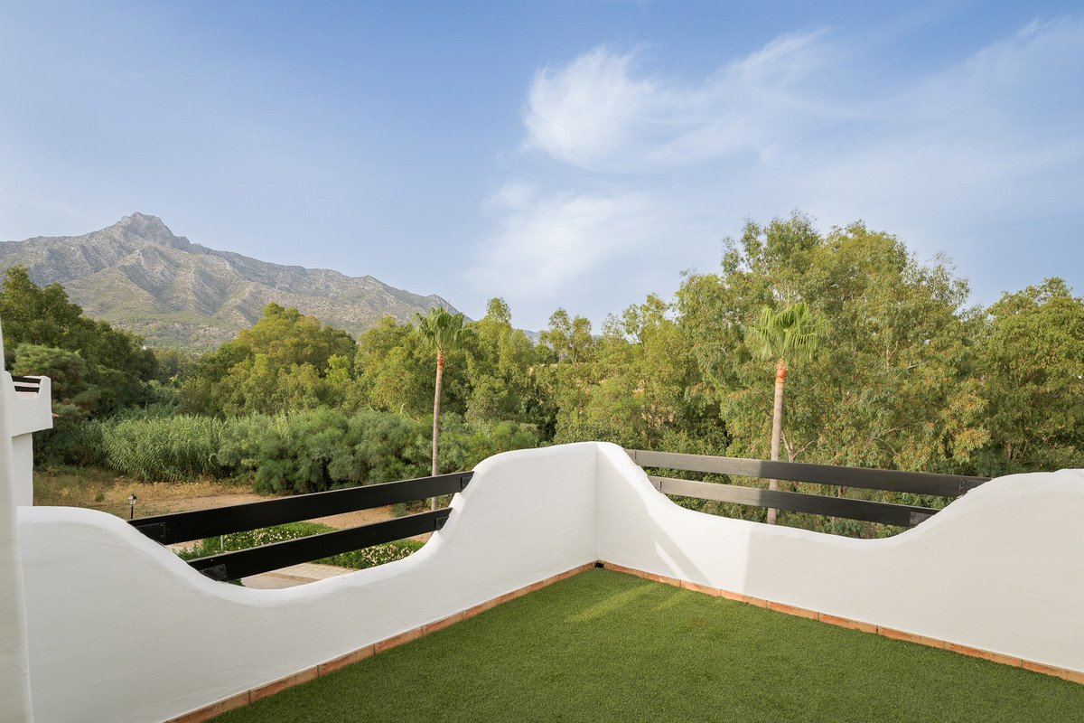 A terrace with artificial grass, white walls, and a view of mountains and trees.