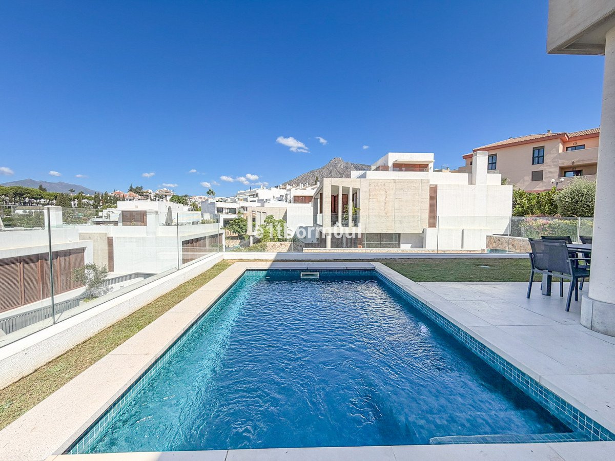 Luxurious modern villa with a private swimming pool, a manicured lawn, and a distant mountain view under a clear blue sky.