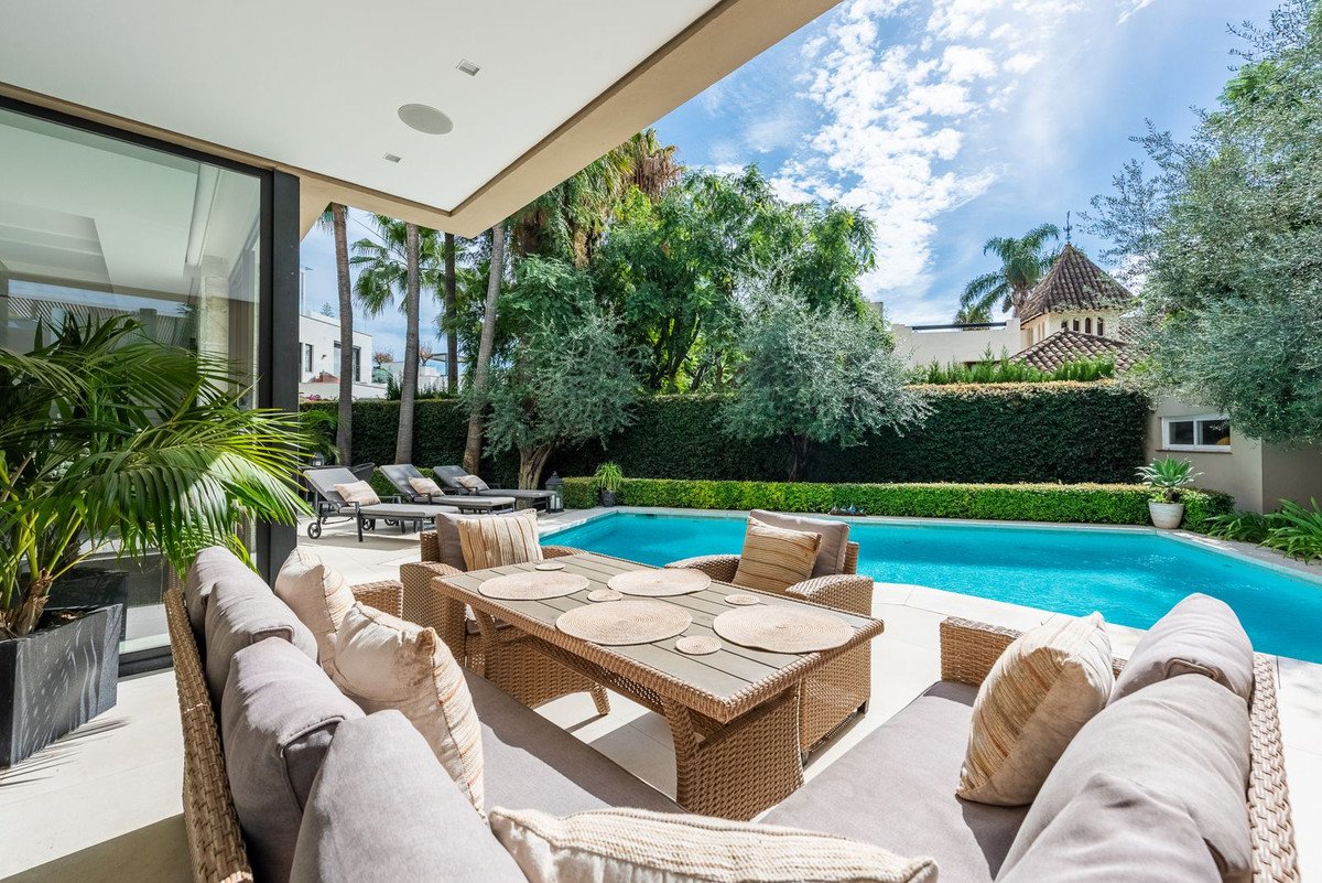 Luxurious patio with comfortable seating, outdoor dining set, and a sparkling swimming pool surrounded by lush greenery.