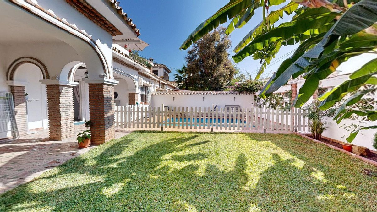 Backyard with green lawn, white picket fence, and swimming pool behind it