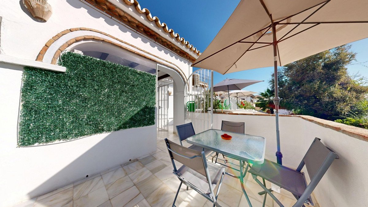 A bright terrace with a glass table, chairs, and a large umbrella.