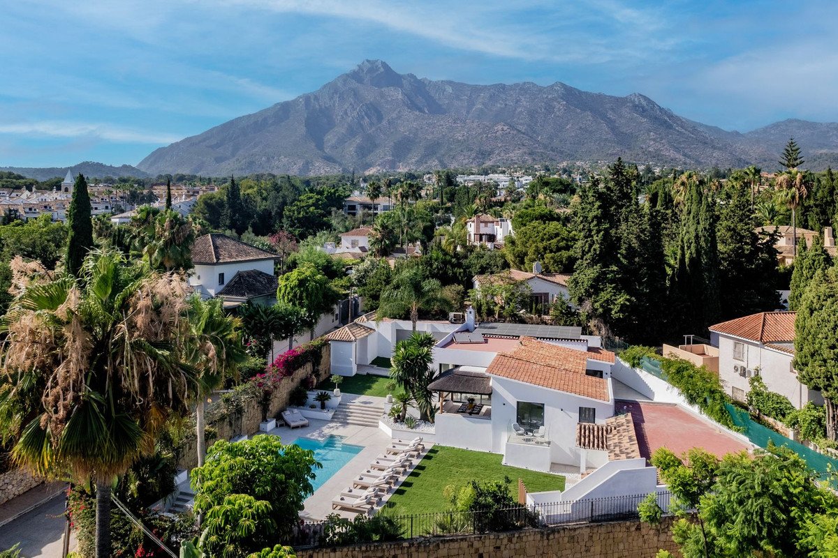 Luxury villa with a swimming pool and sun loungers, set against a backdrop of lush greenery and a majestic mountain.