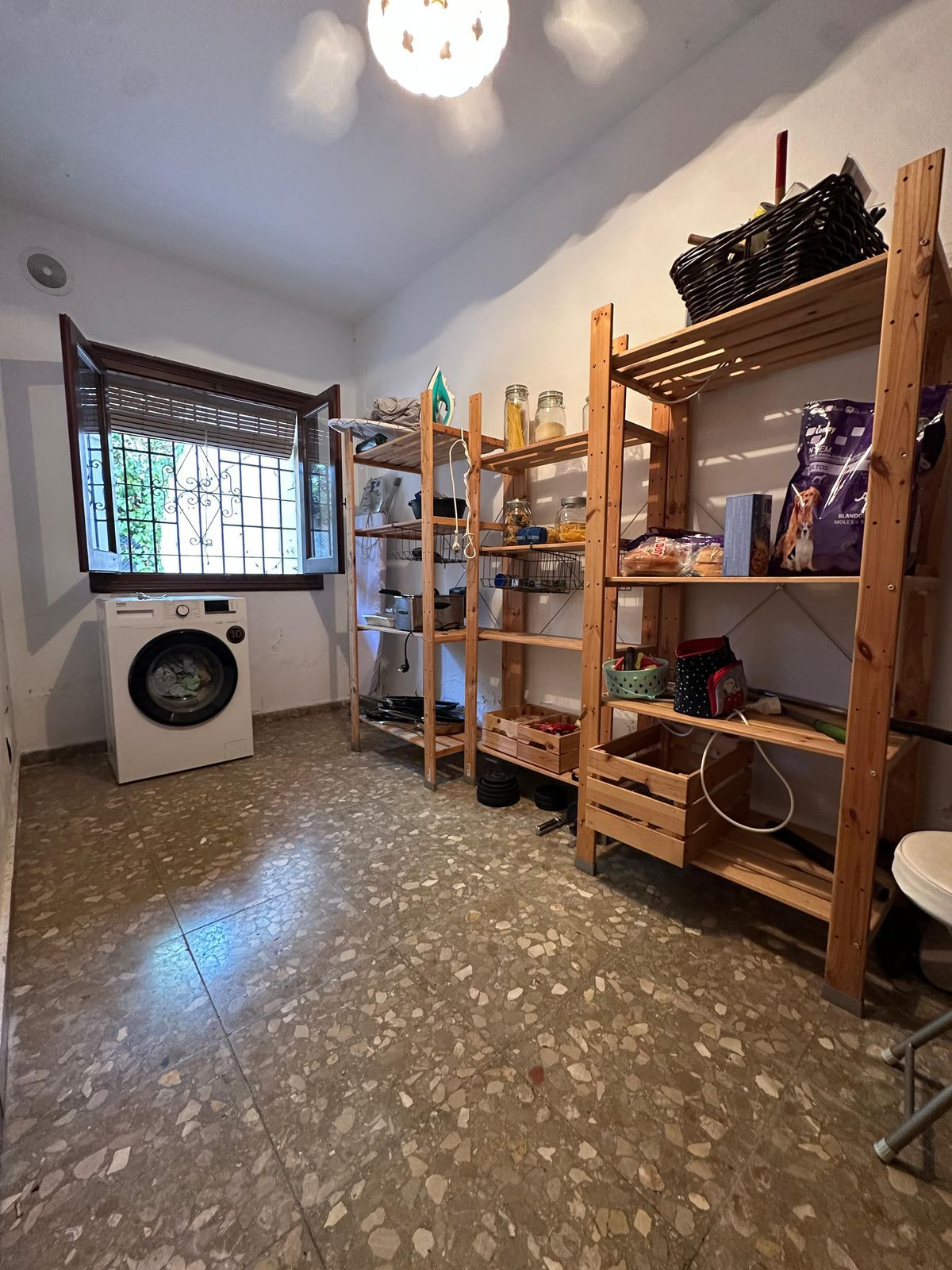 Bijkeuken met wasmachine en houten stellingkasten vol spullen.