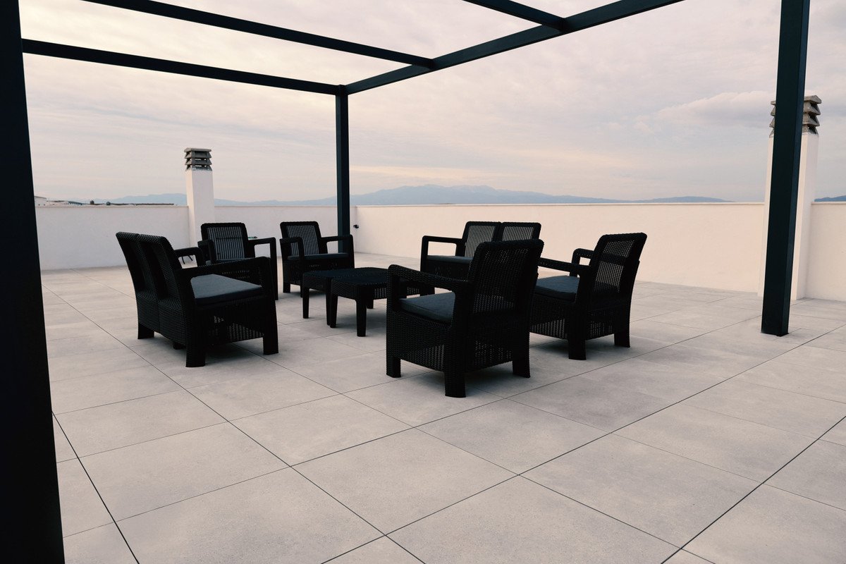 Modern outdoor lounge area with comfortable seating, coffee table, and a distant view of the sea and mountains under a cloudy sky.