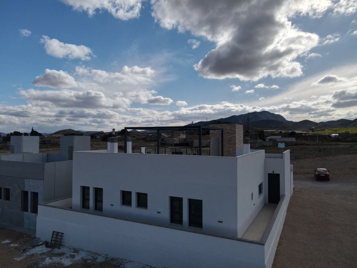 A modern villa under a cloudy sky with a mountain range in the background.
