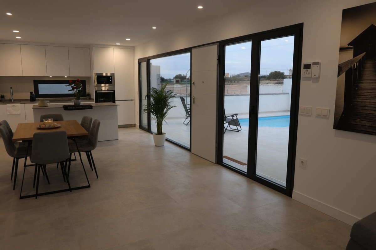 Modern open-plan living space with a kitchen, dining area, and sliding doors leading to a blue swimming pool.