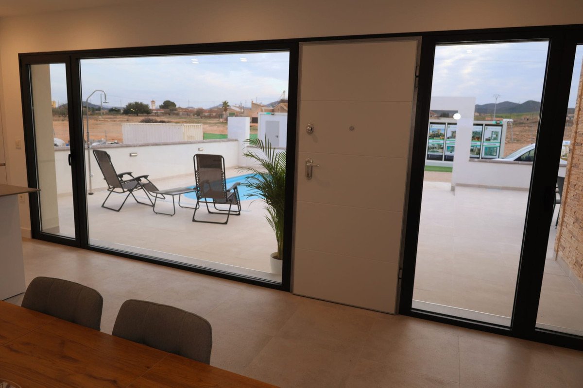 Modern living room with large windows overlooking a patio with a swimming pool and lounge chairs.