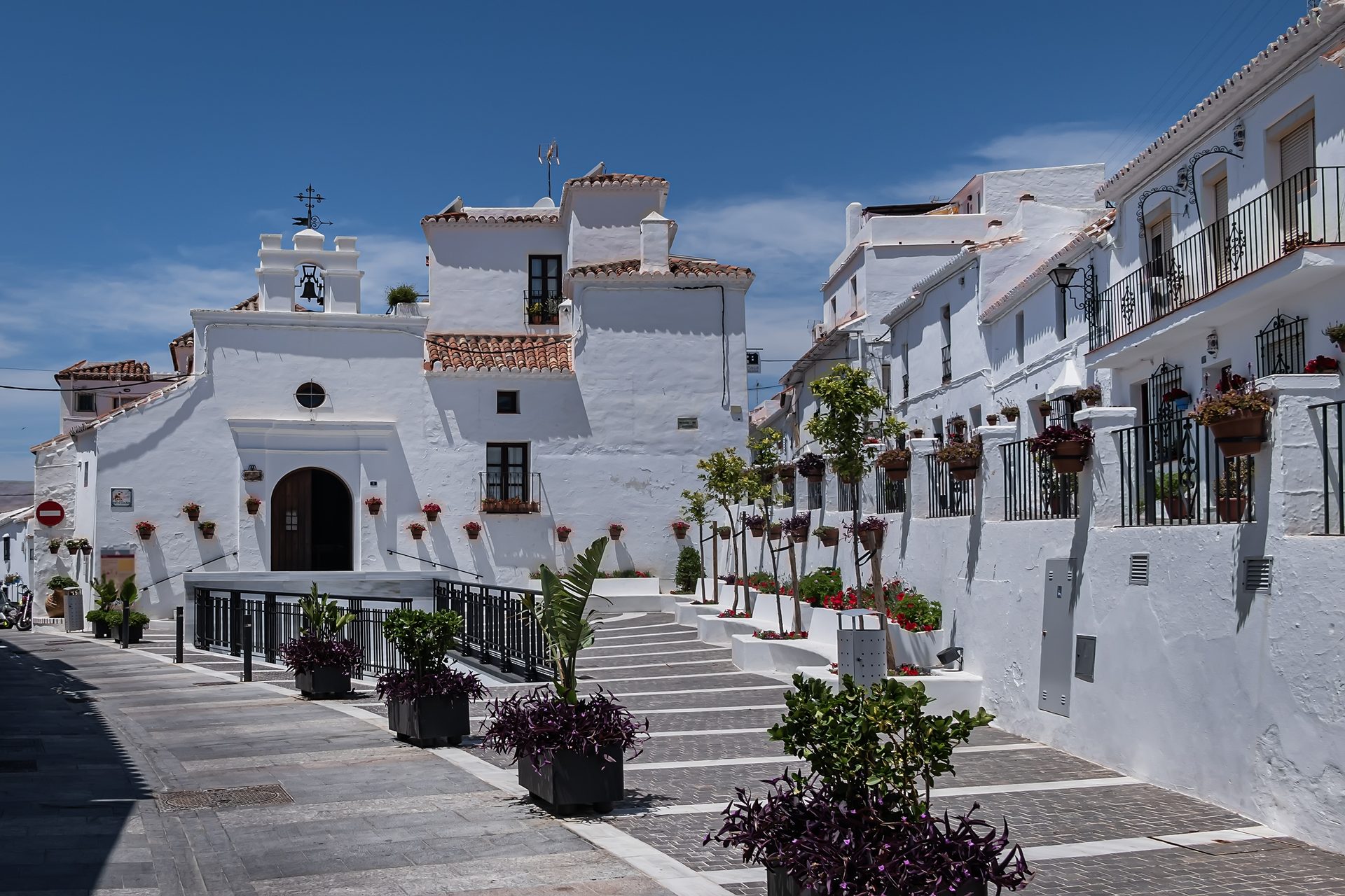 White-walled building with terracotta roof, balconies, and potted plants.