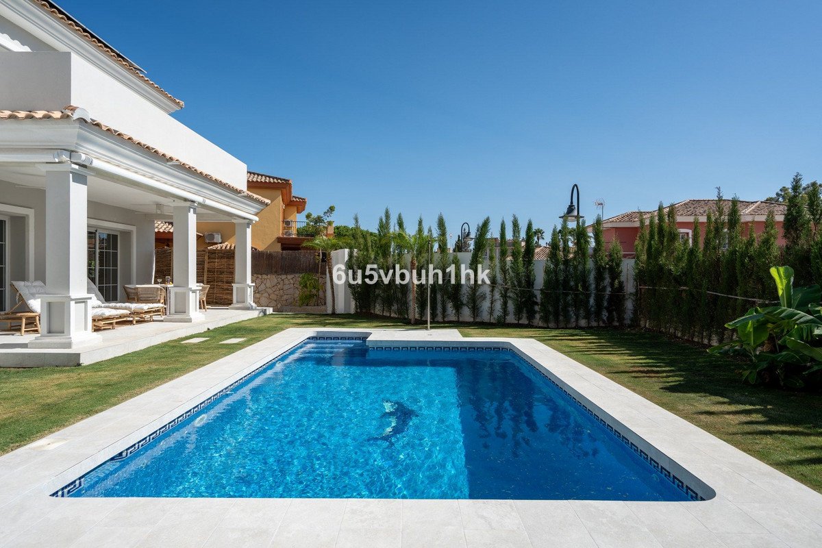 A rectangular swimming pool with a mosaic dolphin in the center, adjacent to a modern villa with a patio and green lawn.
