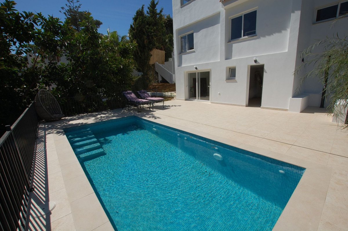 A modern villa with a private swimming pool and tiled terrace, surrounded by lush greenery and lounge chairs.