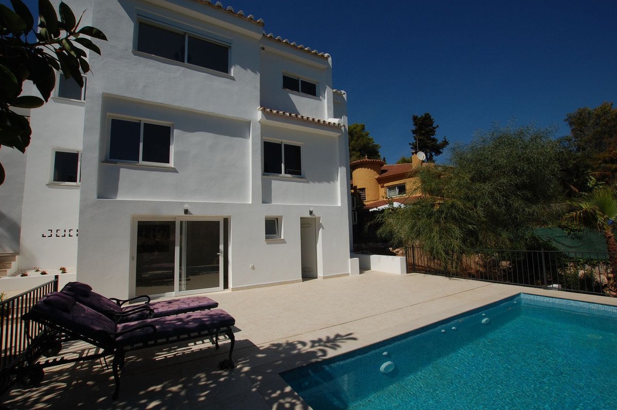 Modern white villa exterior with a swimming pool and sun loungers on the terrace under a clear blue sky.