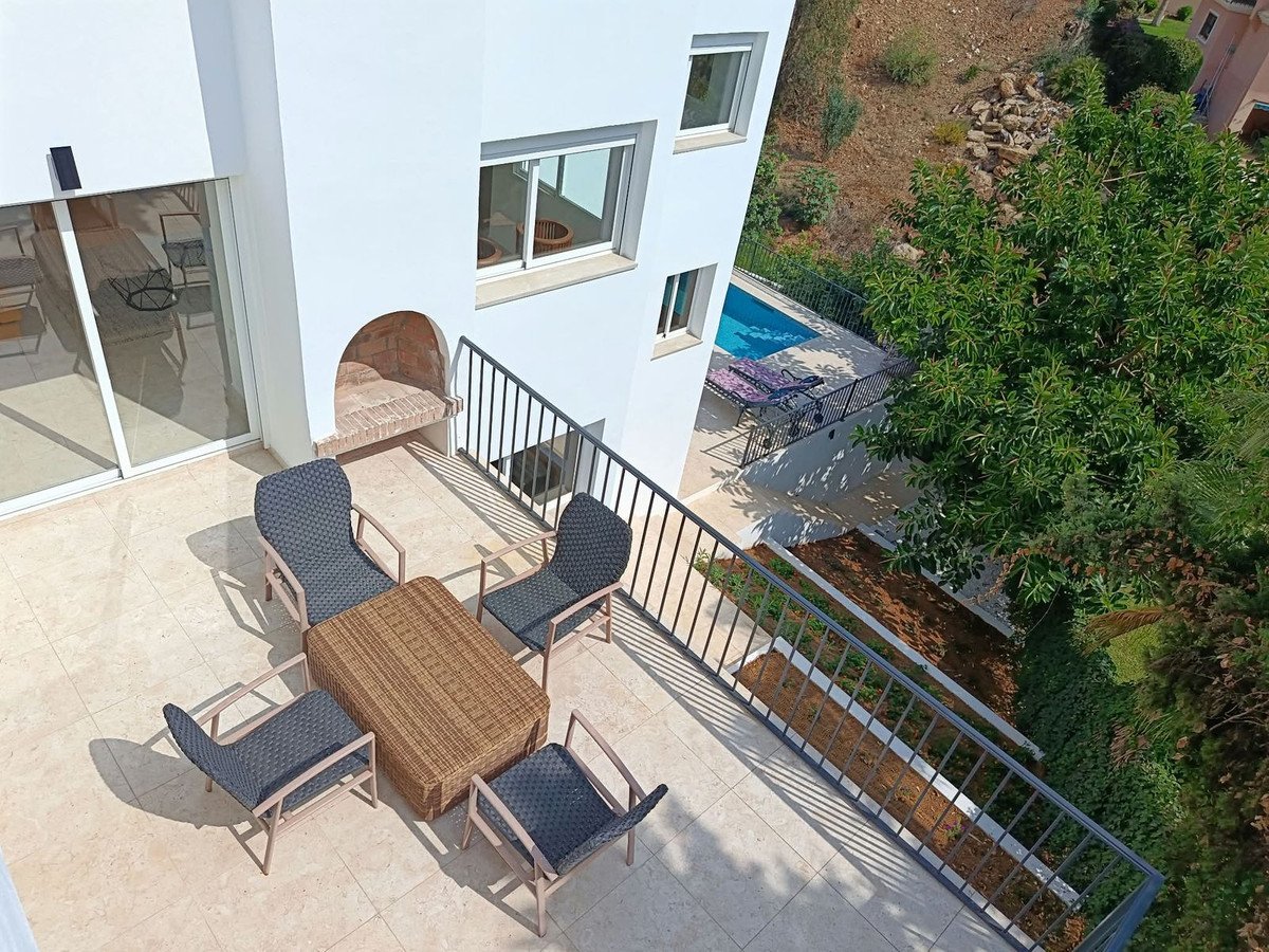 A spacious terrace with outdoor furniture, a built-in barbecue, and a view of the swimming pool and surrounding greenery.