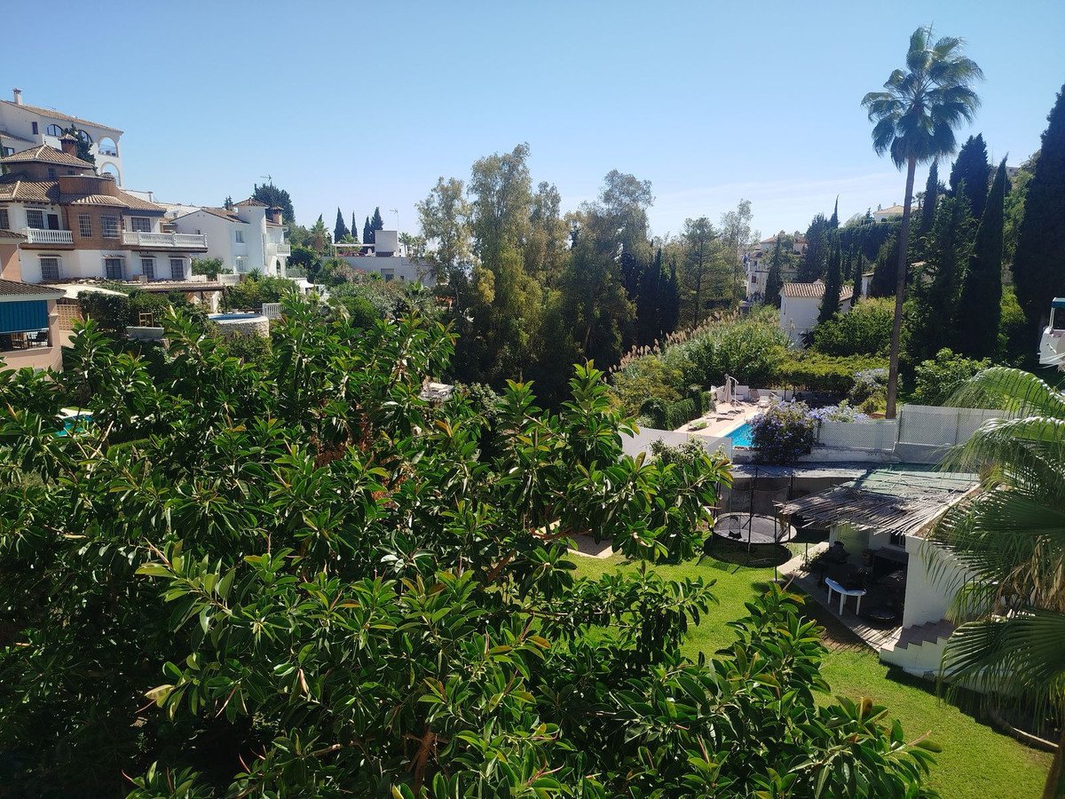 Overlooking a lush garden with a swimming pool and villas in the background on a sunny day.