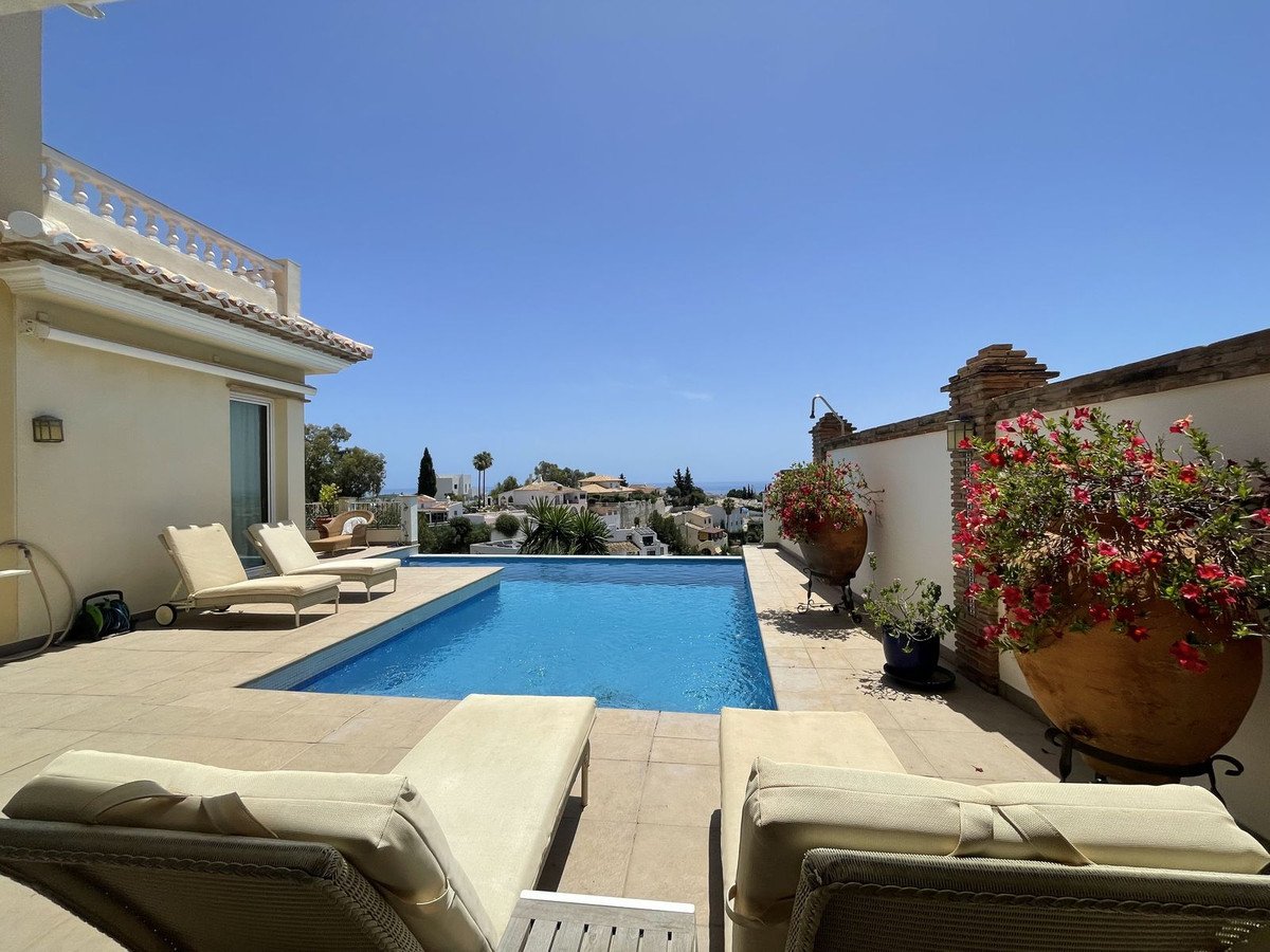 Spacious terrace with a swimming pool, sun loungers, and potted flowers overlooking the sea.