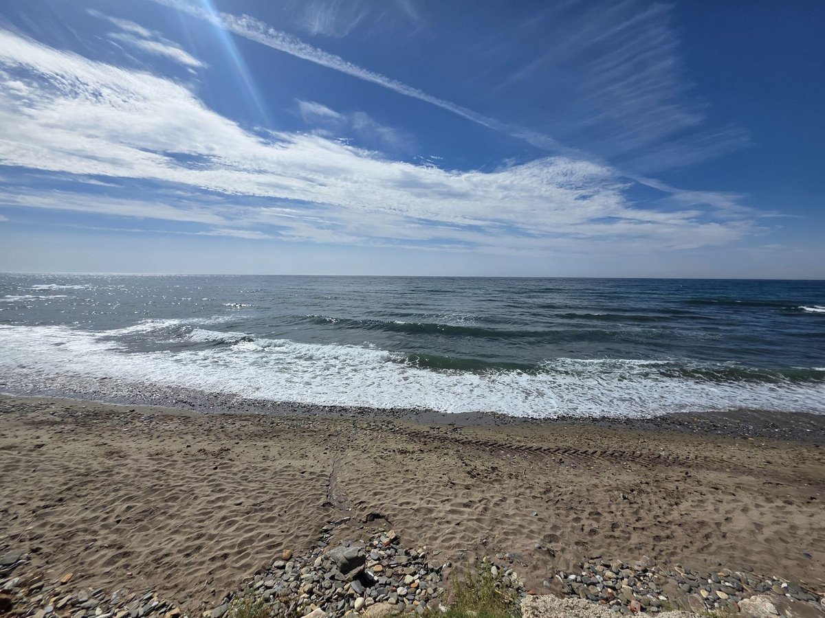 Sandy beach with gentle waves rolling onto the shore under a bright blue sky with scattered clouds.