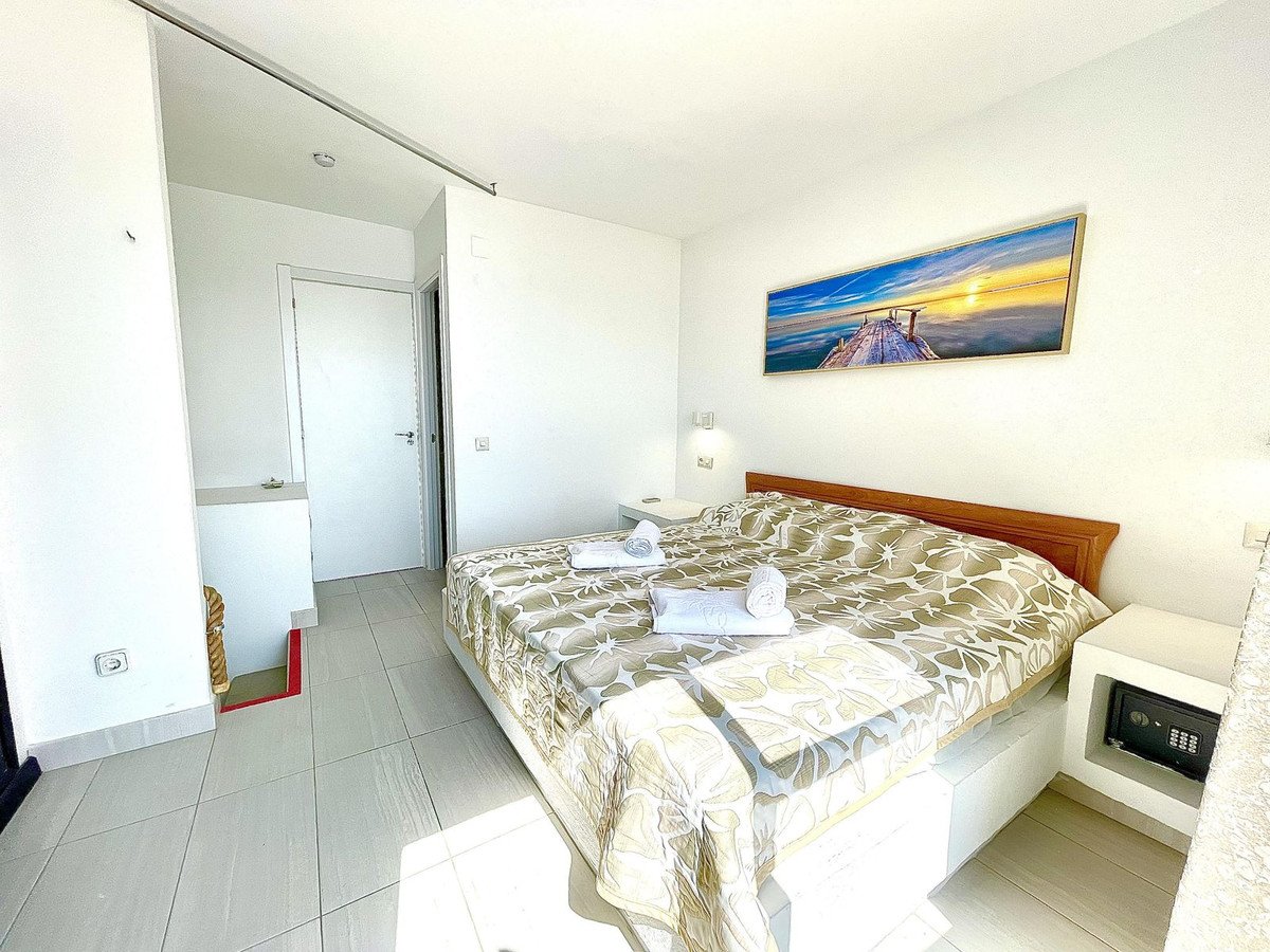 Bright bedroom with a large bed, artwork of a pier at sunset, and a safe on the nightstand.