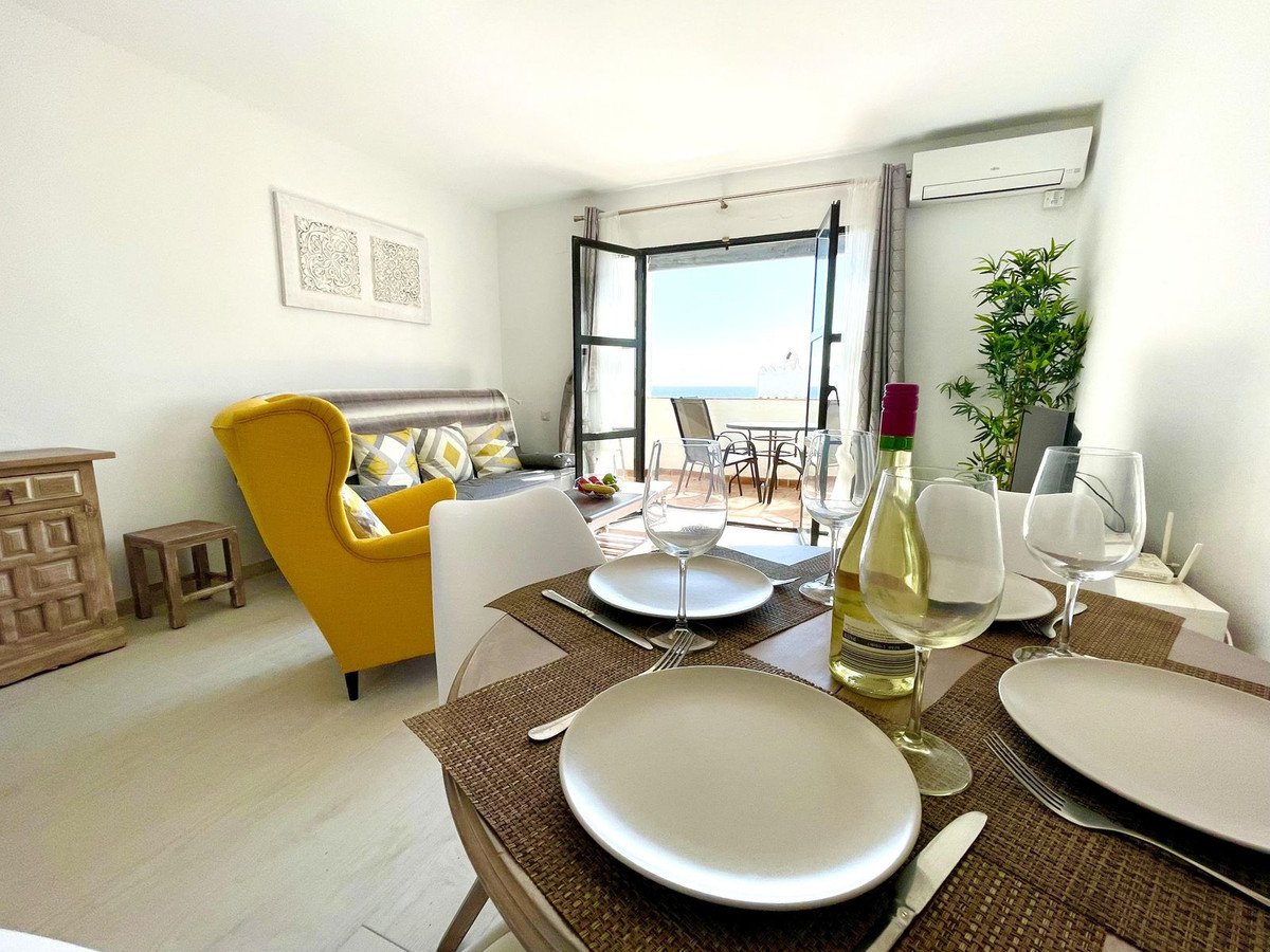 A dining table set for two with wine glasses and a bottle of white wine, leading to a balcony with a sea view.