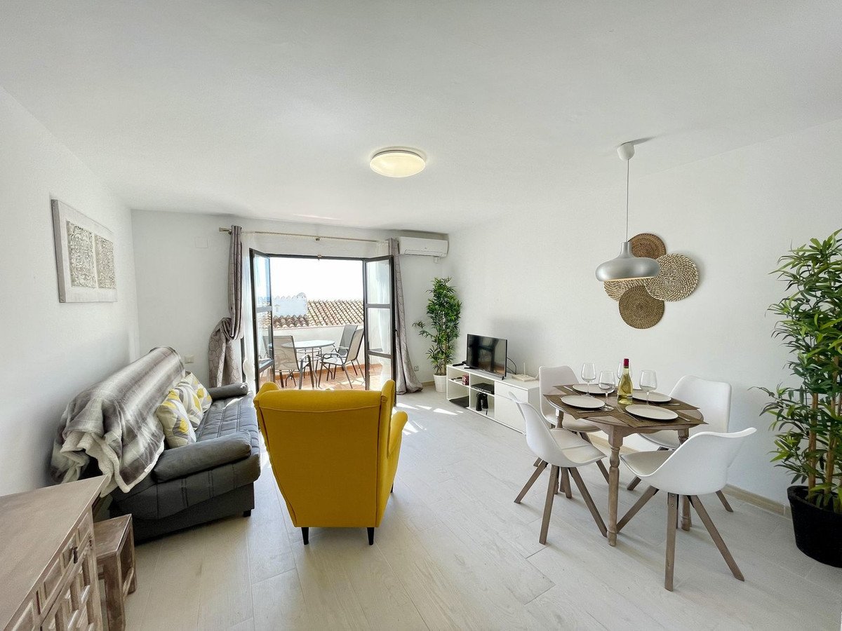 Modern living and dining area with a sofa, armchair, TV, dining table, and access to a terrace with rooftop views.