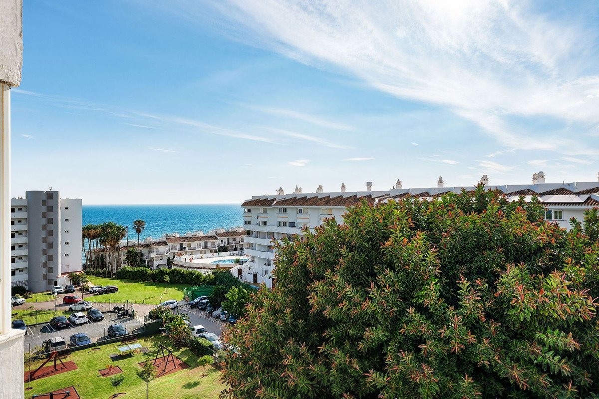 Apartment balcony overlooking the sea with nearby buildings and greenery