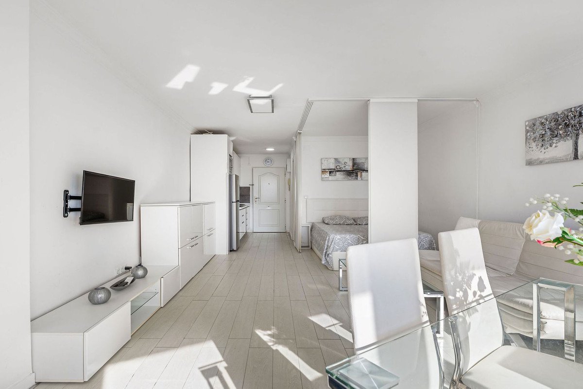Modern studio apartment with open-plan living, white furniture, and bright lighting.
