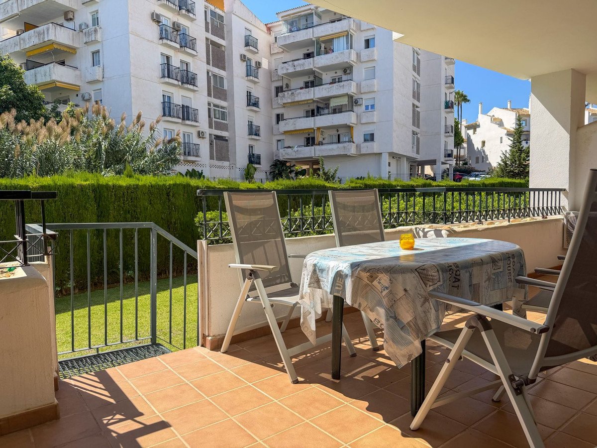 A sunny terrace with a table and chairs overlooking a manicured garden and apartment buildings.