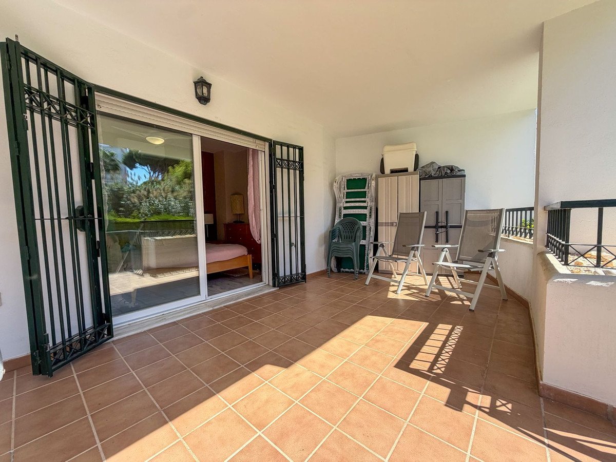 Terrace with chairs, garden view through glass doors, and storage units. Includes a glimpse of a bedroom.