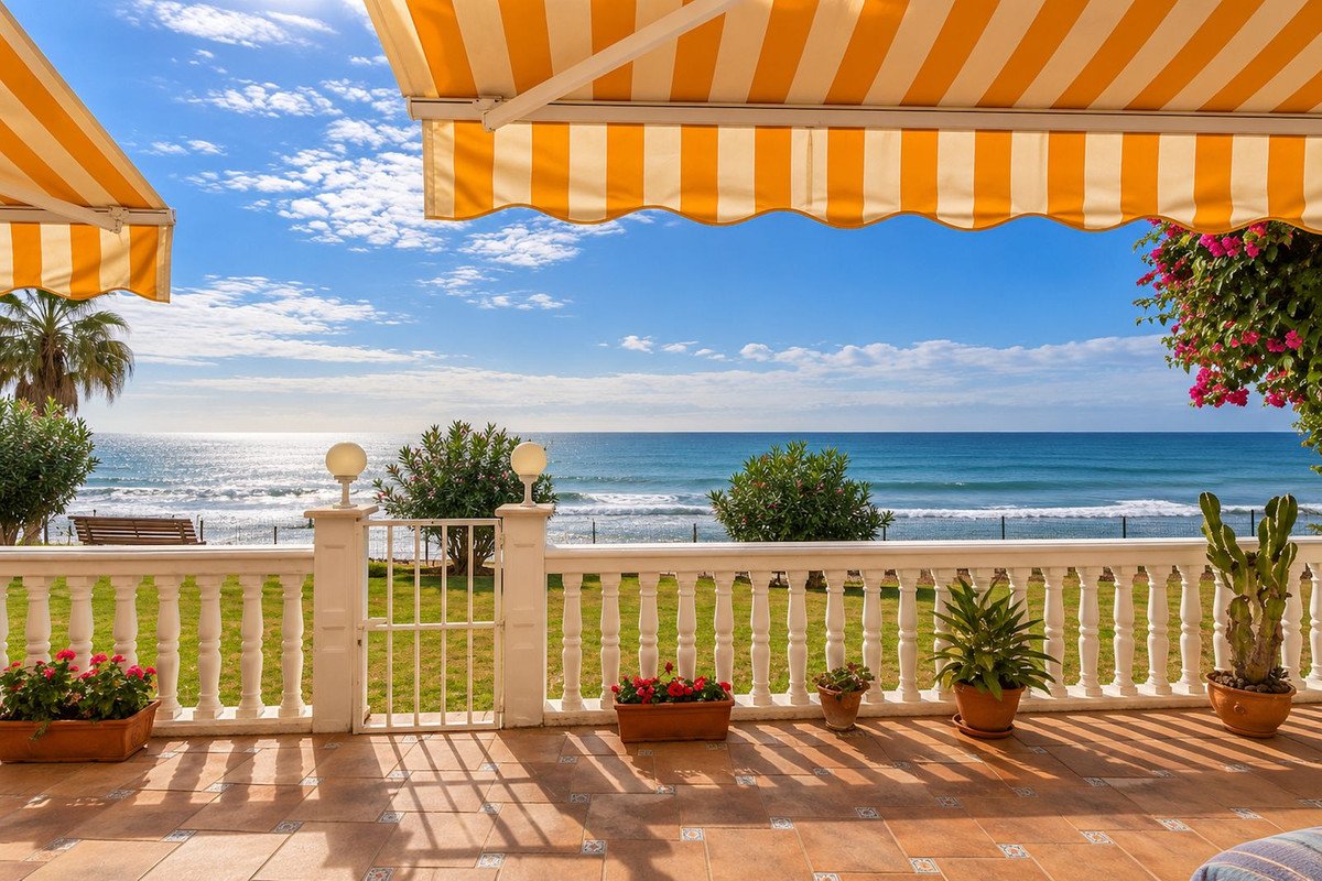 A sunny terrace with striped awnings offers a beautiful sea view with green grass and potted plants.