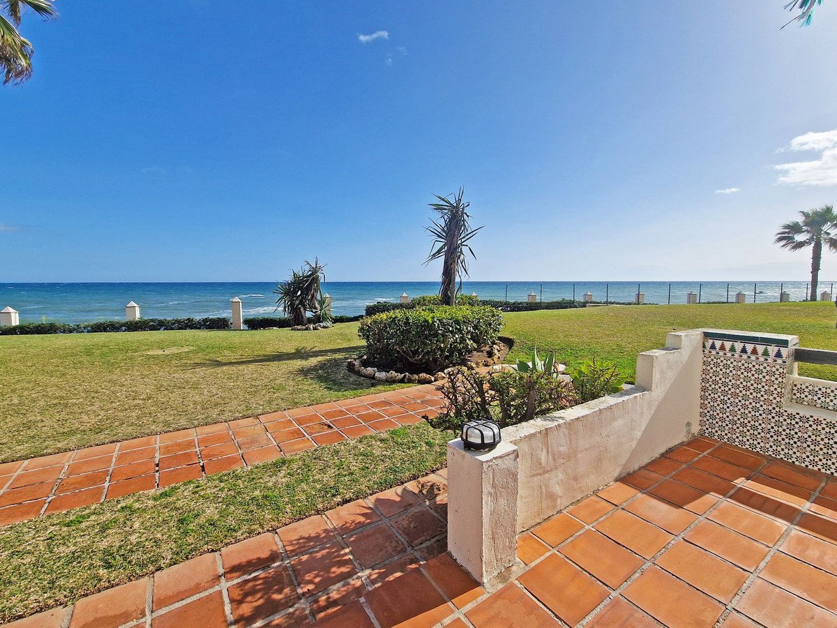 Terracotta tiled patio with a lush green lawn leading to the ocean and a clear blue sky.