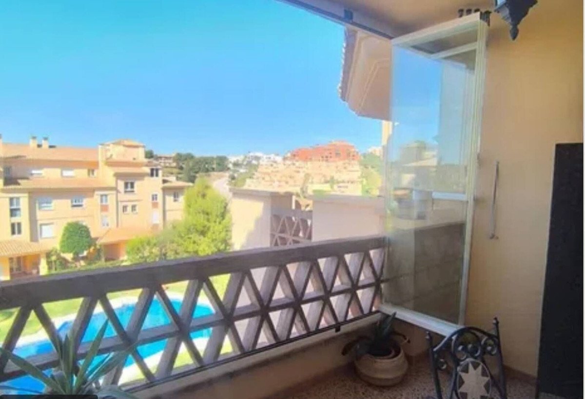 Balcony view overlooking a swimming pool and apartment buildings under a clear blue sky.