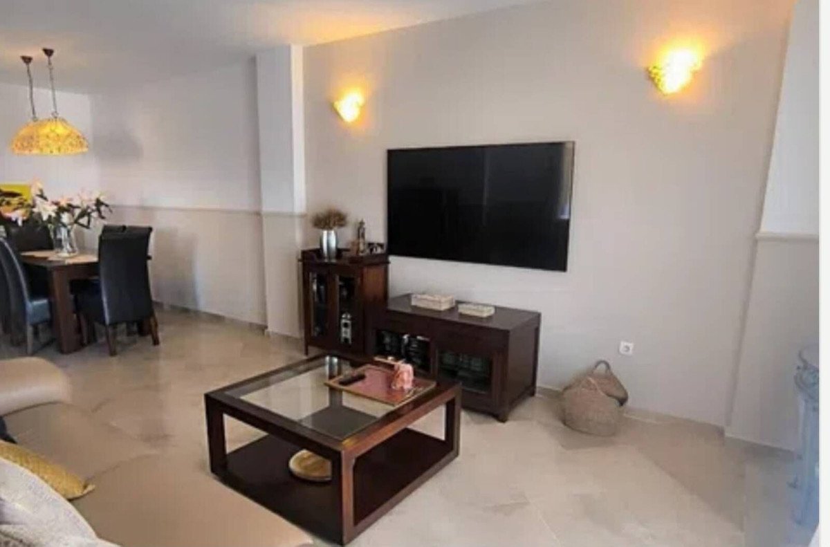Spacious living and dining area with a large TV, coffee table, dining set, and ambient wall sconces.