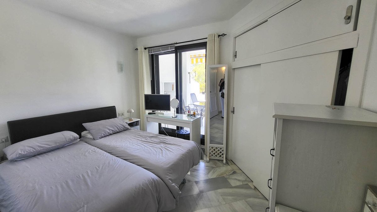 Bedroom with two beds, a desk with a TV, and a sliding door leading to a balcony with outdoor seating.