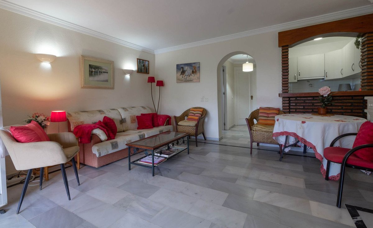 Comfortable living and dining area with sofas, chairs, coffee table, and dining table, featuring bright decor and arched entryway to kitchen.