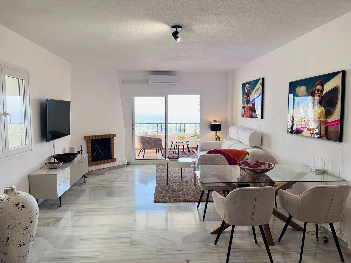 Living and dining area with sea view, fireplace, terrace access, and modern decor.