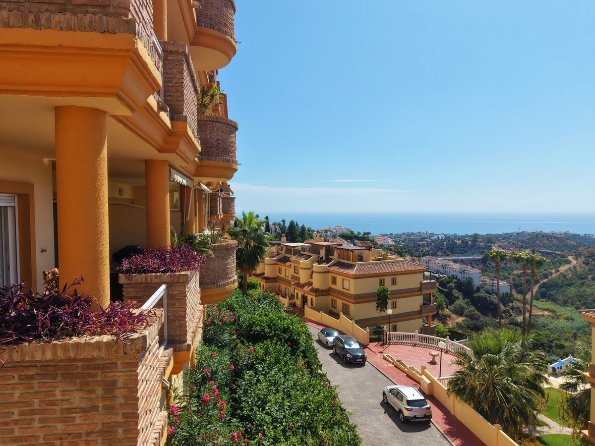 View from a balcony with the sea and town in the distance, overlooking buildings and greenery on a sunny day.