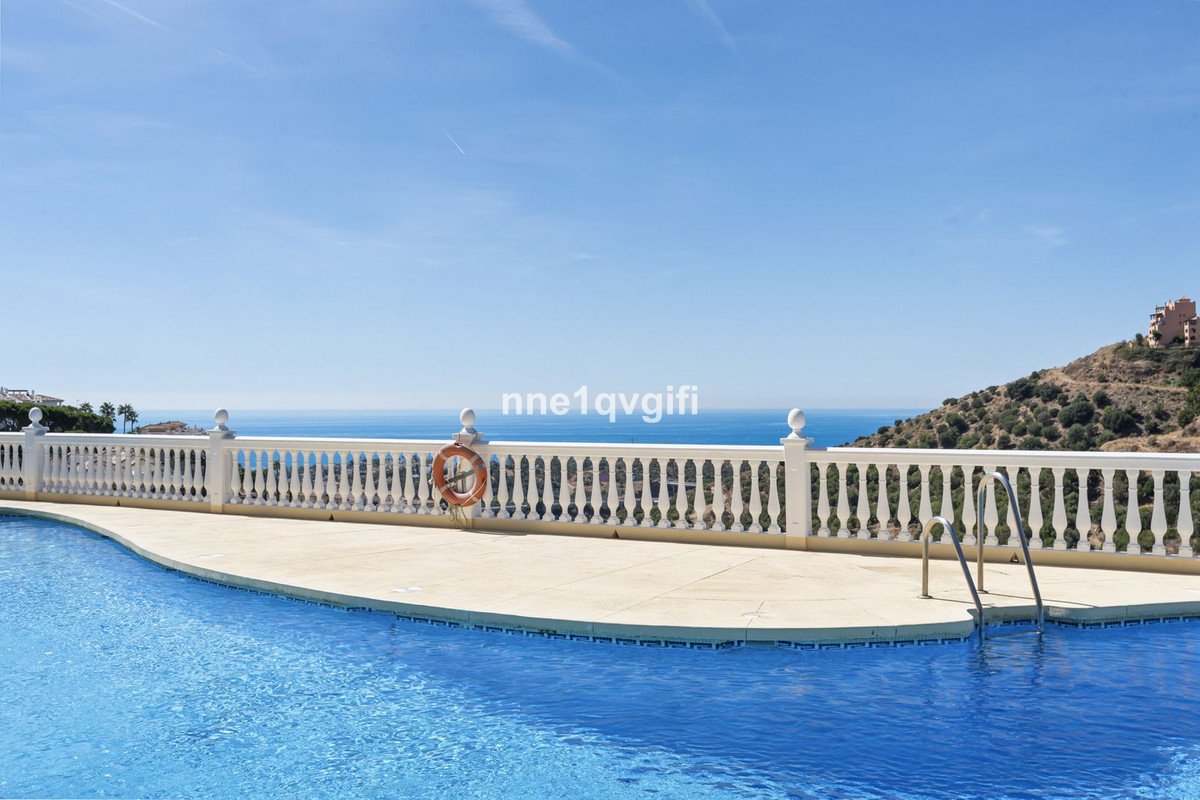 A swimming pool and terrace with a white balustrade overlooking the sea on a sunny day.
