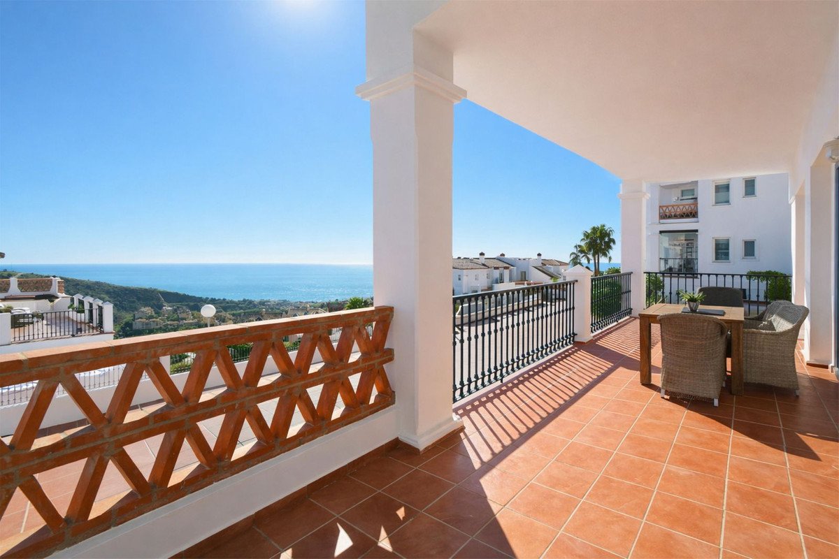 Spacious balcony with sea views, featuring a dining table and chairs on a tiled terrace under a clear blue sky.