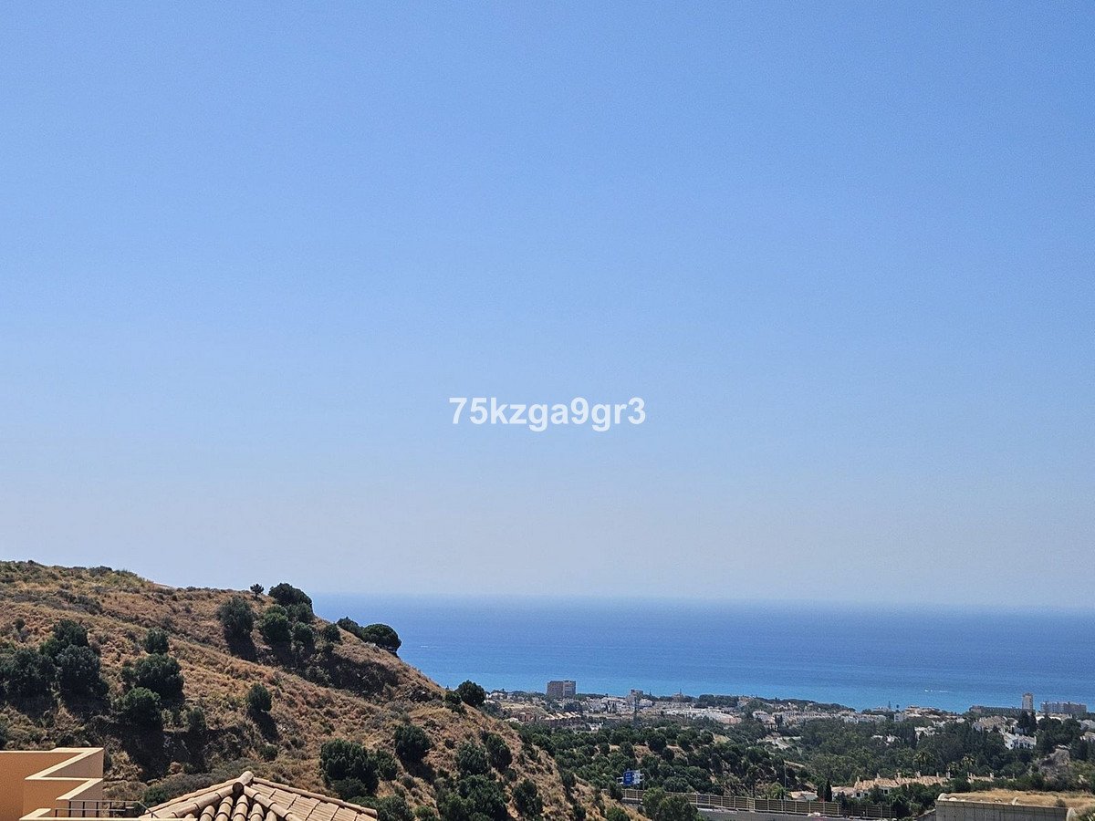 Coastal view with sea, hills, and distant town under clear sky