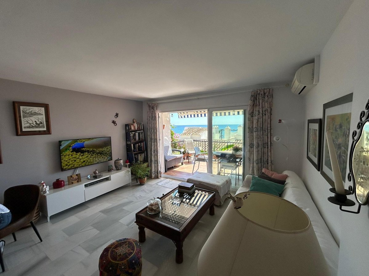 Spacious living room with a white sofa, coffee table, and a balcony overlooking the sea and coastline.