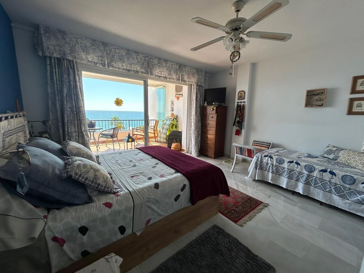 Bedroom with a large bed, a single bed, and a balcony overlooking the blue sea and a sunny sky.
