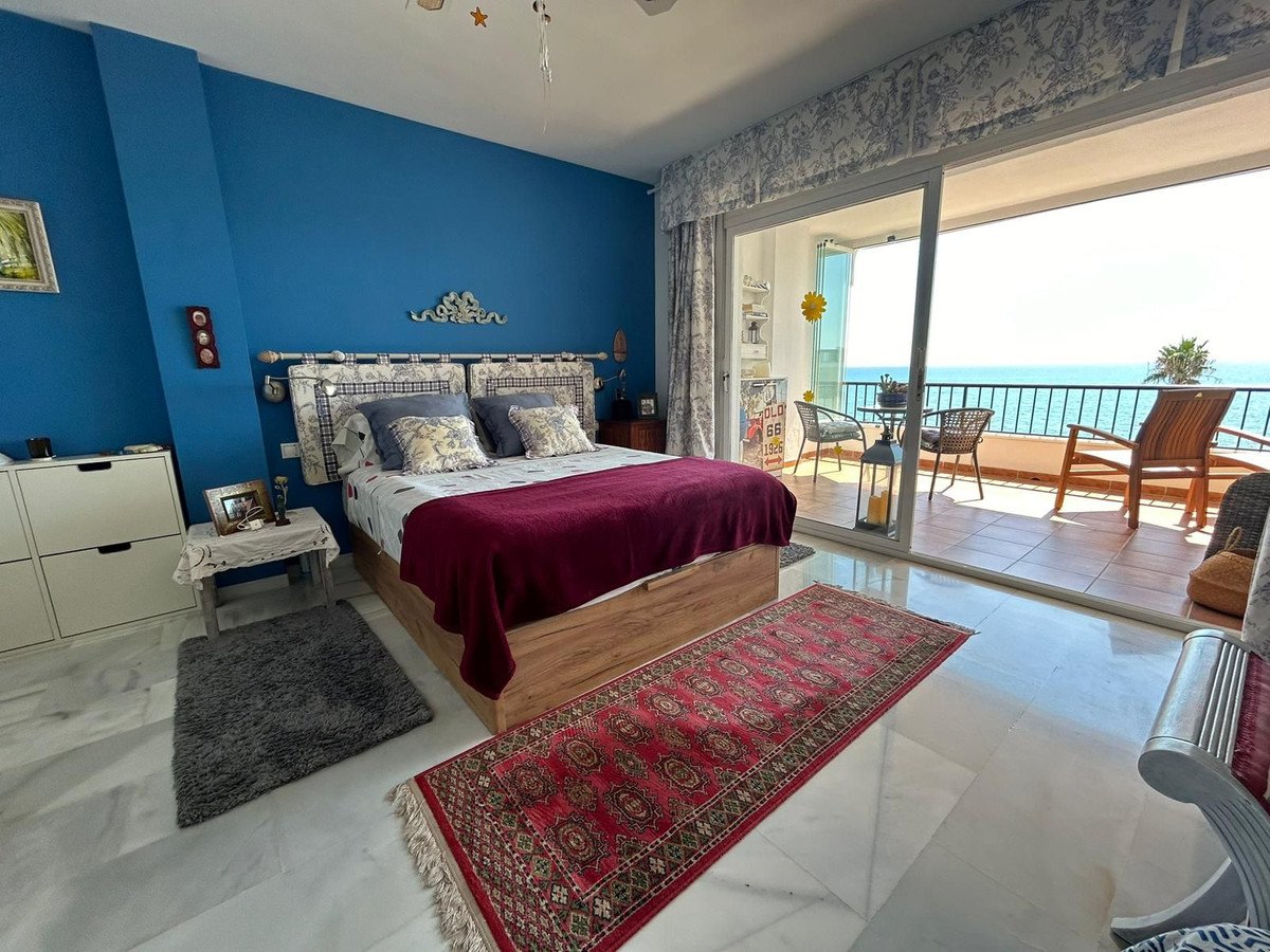 Spacious bedroom with a king-size bed, blue walls, and a balcony offering a stunning sea view.