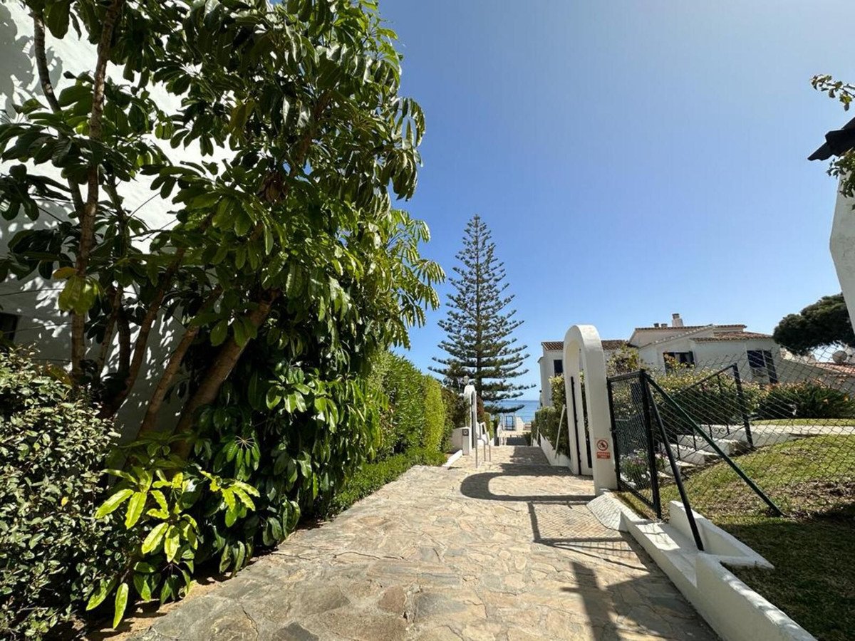 Stone pathway leading to a villa, with lush greenery and a distant sea view under a clear blue sky.